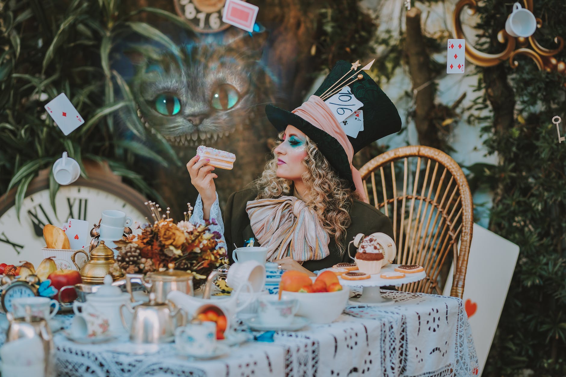 female mad hatter eating a cake amid floating cups and playing cards